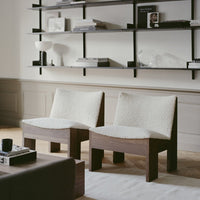 Two cozy chairs featuring soft white upholstery and rich wooden frames, set against a neutral-colored backdrop.
