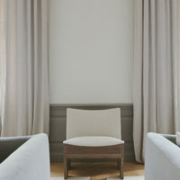 Neutral beige chair with textured upholstery, surrounded by soft gray hues and light-toned curtains in a minimalist setting.
