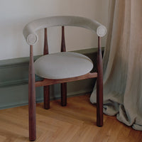 Chair with wooden frame and light gray cushion against a neutral wall.