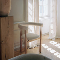 Minimalist chair with wooden frame and white cushion in a softly lit room.
