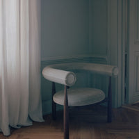 Modern chair with curved backrest in a room with light blue walls and white curtains.