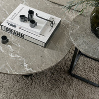 "Round gray marble coffee tables with subtle veins, complemented by a black book and decor on a textured beige rug."