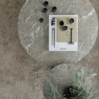 "Round gray marble table with soft beige carpet, featuring black accessories and a stylish magazine for a modern look."