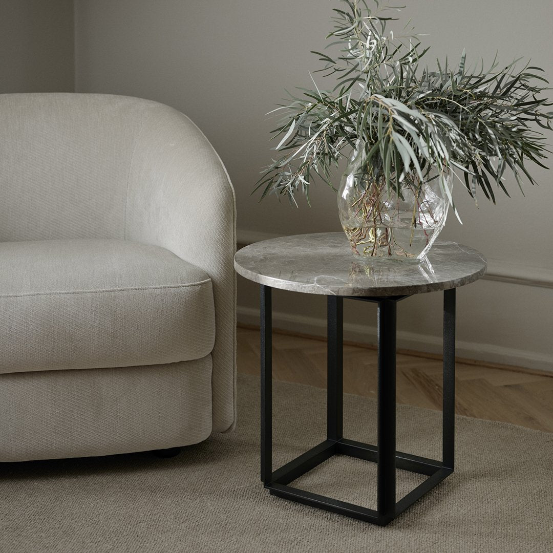 Elegant round marble tabletop in gray with a black metal base, paired with a cozy beige armchair and neutral tones.