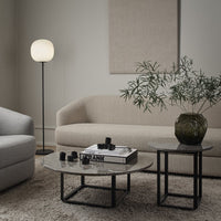 Beige and gray textured sofas, round marble tables, black metal bases, and a green patterned vase in a cozy living room.