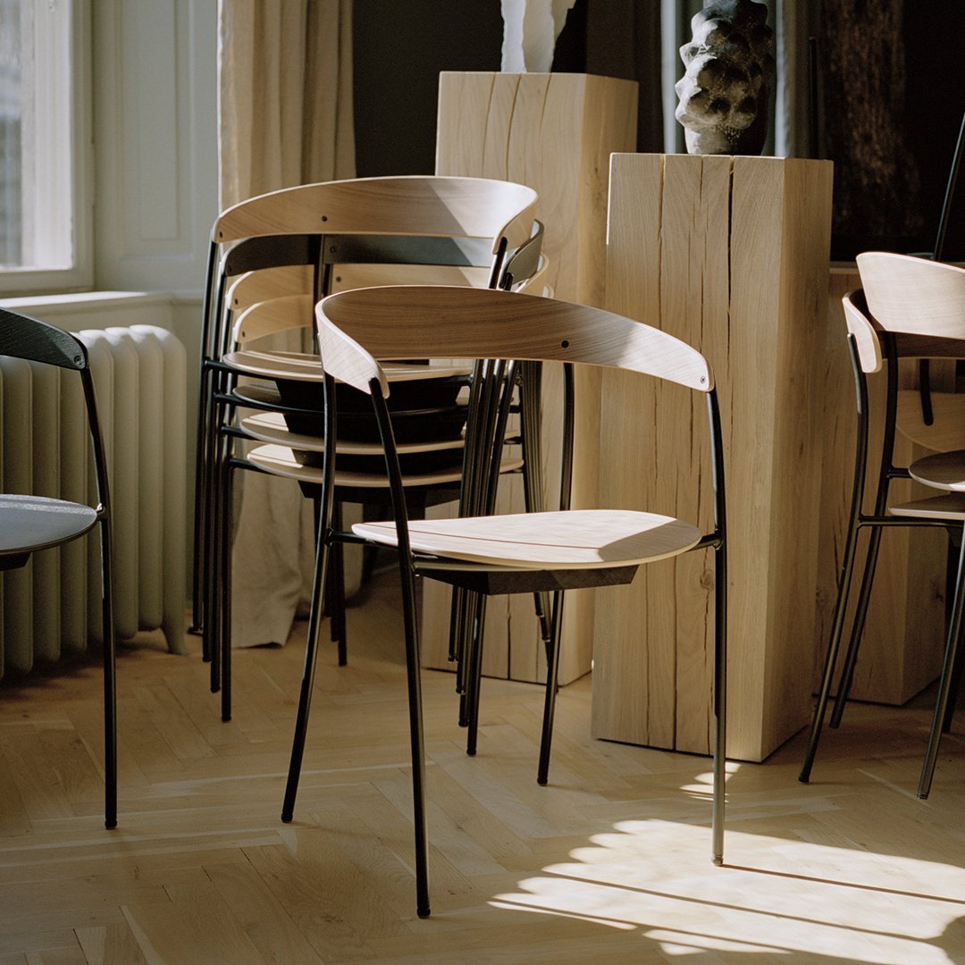 Minimalist black and wood chairs with smooth lines and natural finishes, set against a bright, airy interior.