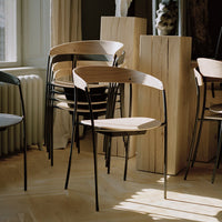 Minimalist black and wood chairs with smooth lines and natural finishes, set against a bright, airy interior.