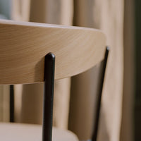 Light wood tabletop with subtle grain pattern and sleek black metal legs, set against soft beige curtains.