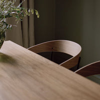Natural wood surface with smooth grain, paired with curved, light-colored chairs in a serene, minimalistic setting.