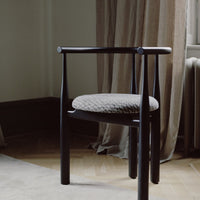 Dark wooden chair with a gray cushion in a room with curtains and a rug.