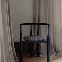 Black chair with a patterned cushion against beige curtains