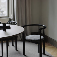 Black chair with a patterned cushion next to a round table in a room with curtains and a window.