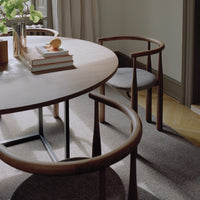 Round dining table with wooden chairs in a room with light-colored walls and carpet.