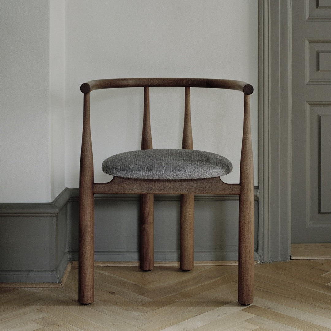 Wooden chair with a gray cushion on a wooden floor against a neutral wall.