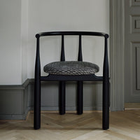 Black chair with a patterned cushion on a wooden floor and light-colored wall.