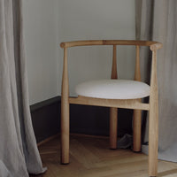 Wooden chair with a white cushion in a room with curtains and wooden floor.