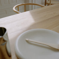 Light wooden table with a pale round plate and a light-colored wooden spatula, featuring soft shadows and smooth textures.