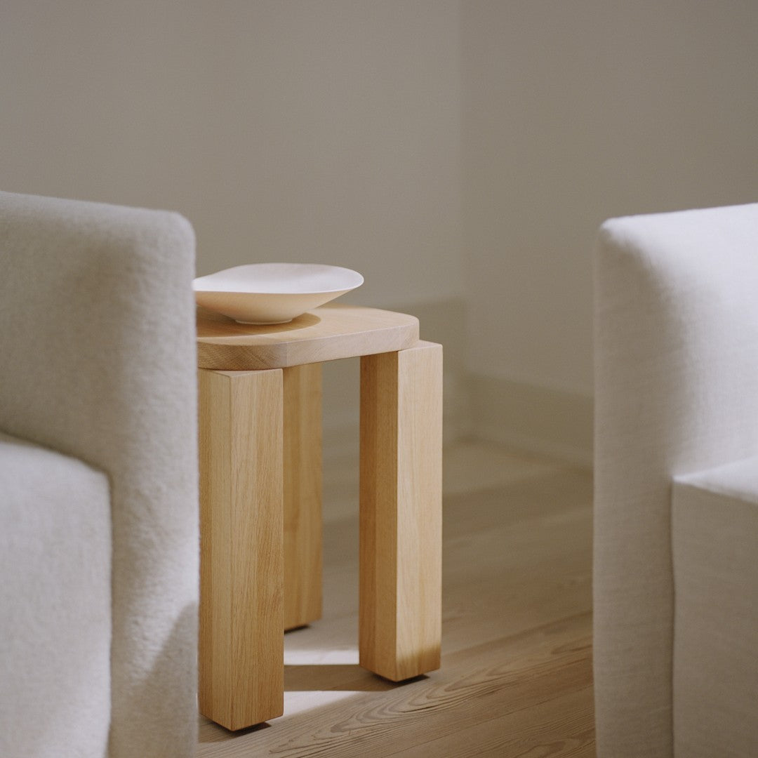 Natural wooden side table with a light beige plate on top, set against soft, neutral background tones.