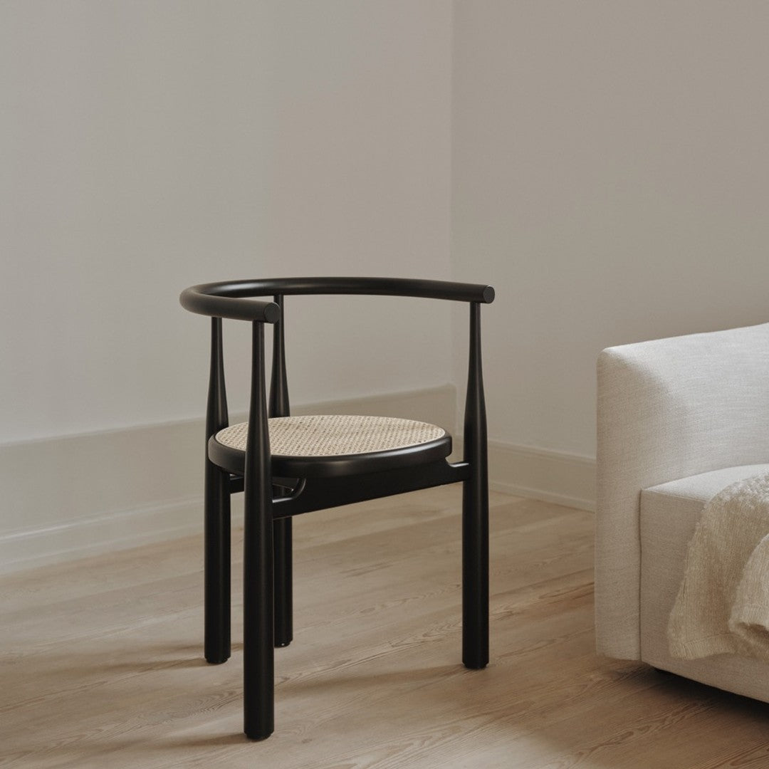 Black wooden chair with a woven cane seat, featuring a minimalist design and neutral tones. Perfect for modern decor.