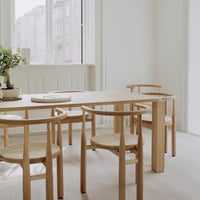Light wood dining table and chairs with natural woven seats, set against a bright, minimalist white background.