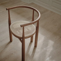Natural wood chair with a round cane seat, featuring a light tan color and a woven texture pattern.