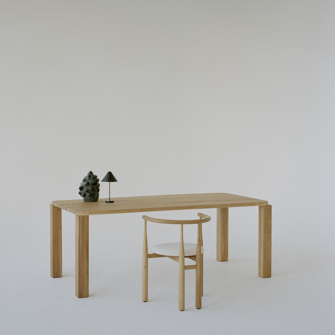 Wooden table and chair in natural tones with minimalistic black and green accents on a light background.