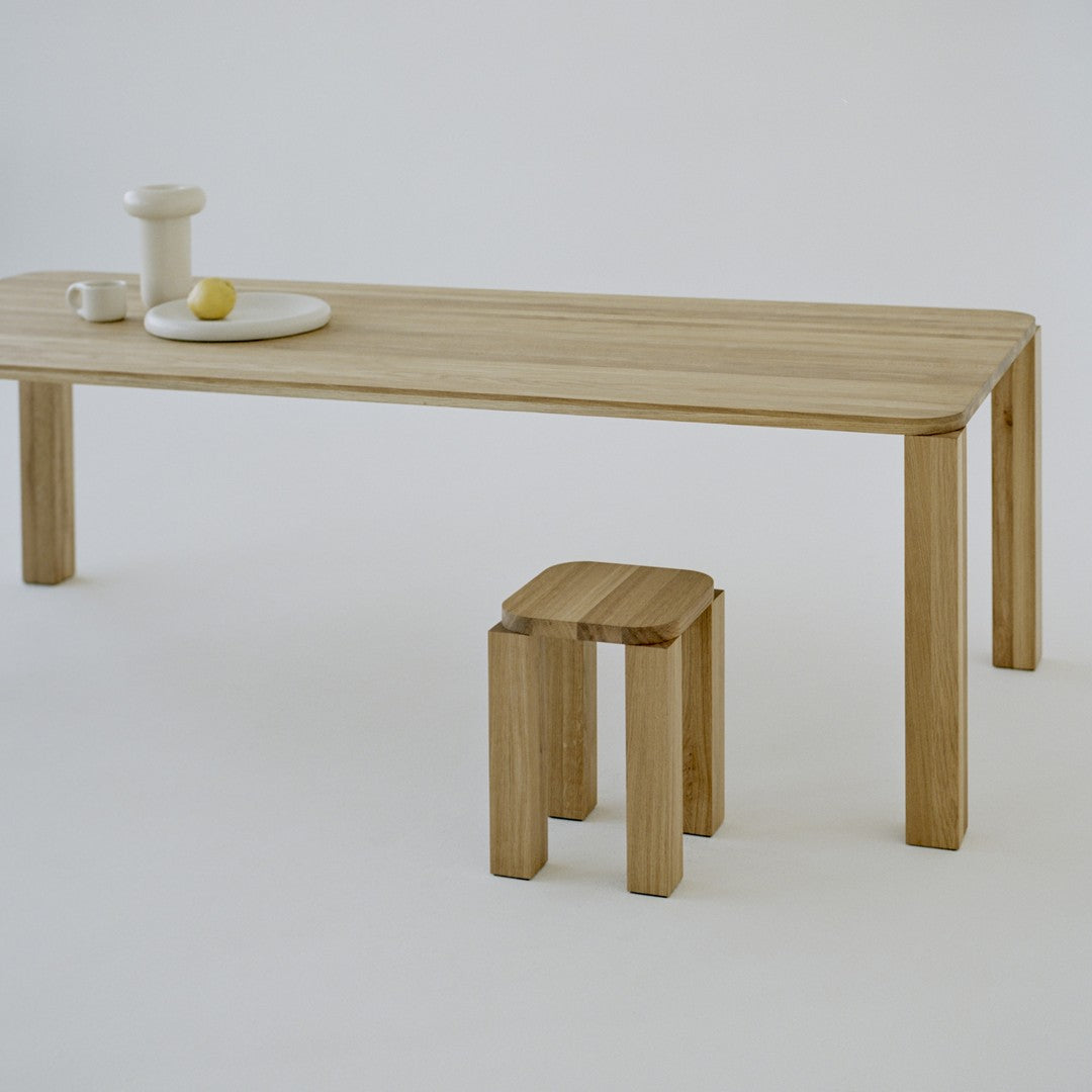 Natural wood grain table and stool with light beige tones, featuring a minimalist design against a white background.