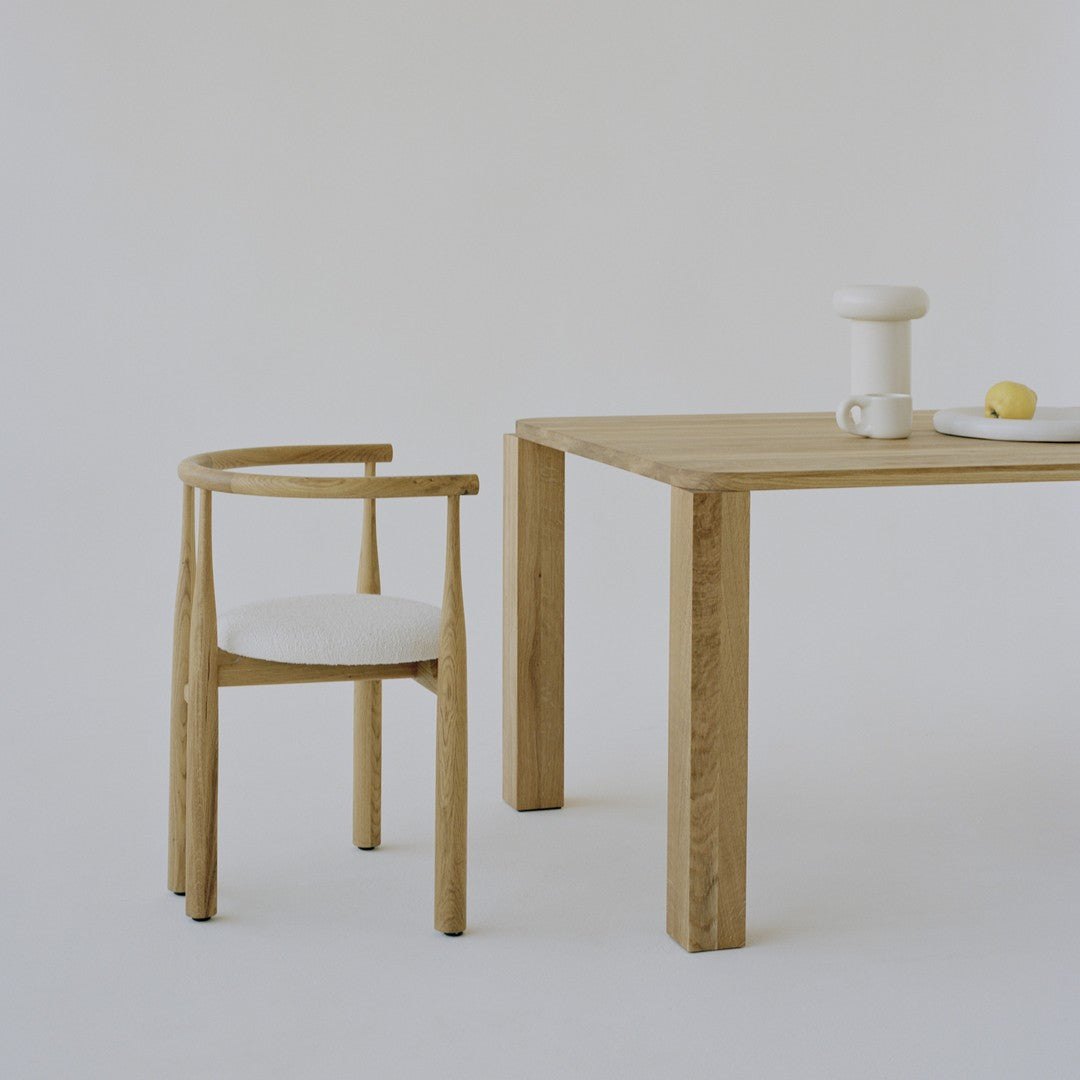 Light wood chair with cream upholstery next to a minimalist wooden table, all set against a neutral backdrop.
