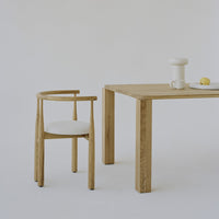 Light wood chair with cream upholstery next to a minimalist wooden table, all set against a neutral backdrop.