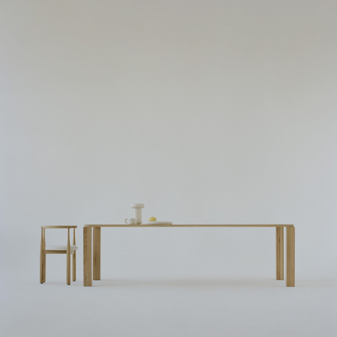 Minimalist light wood table and chair on a soft white background, featuring smooth, clean lines and neutral tones.