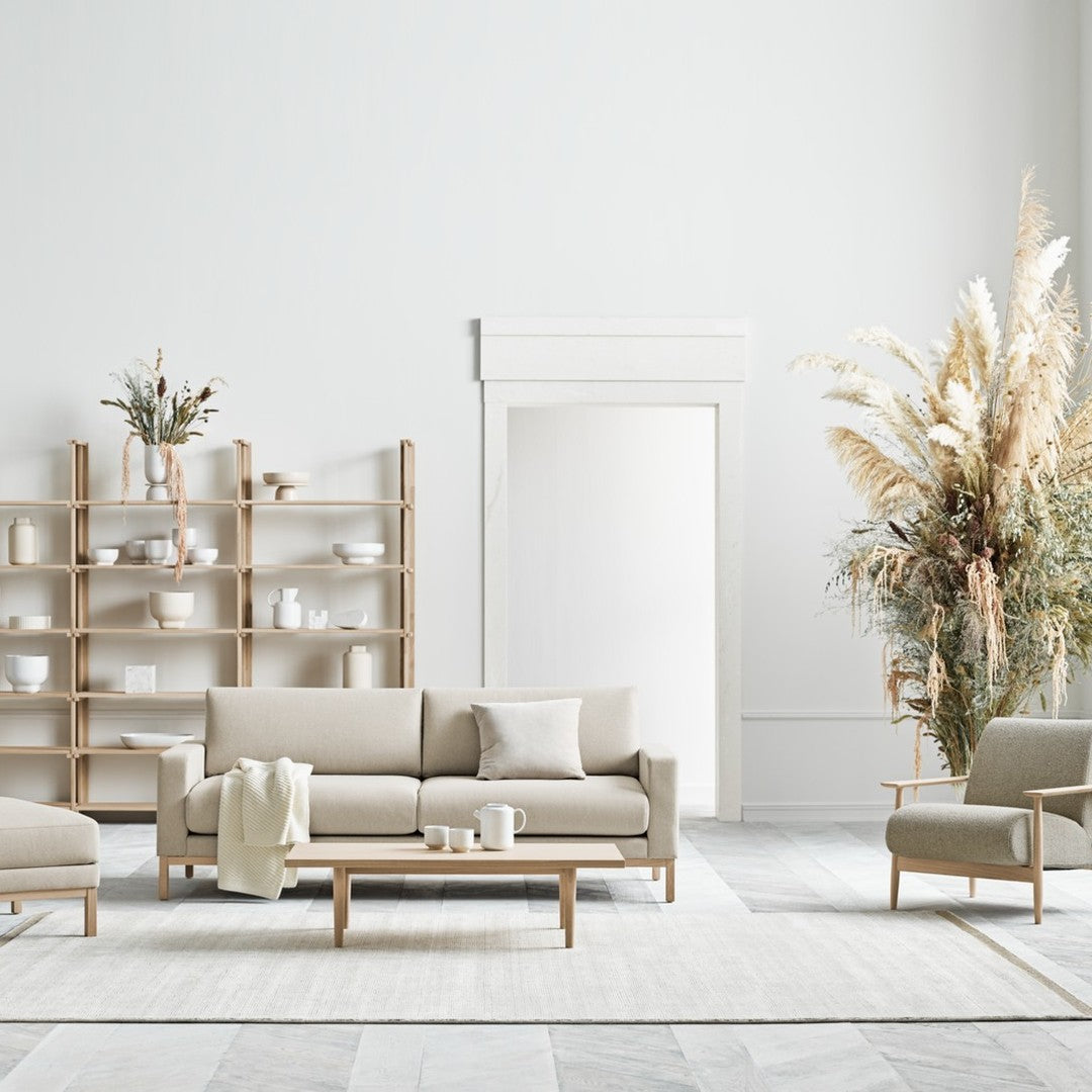 Beige and neutral seating with light wood accents, set against a soft gray and white patterned rug.