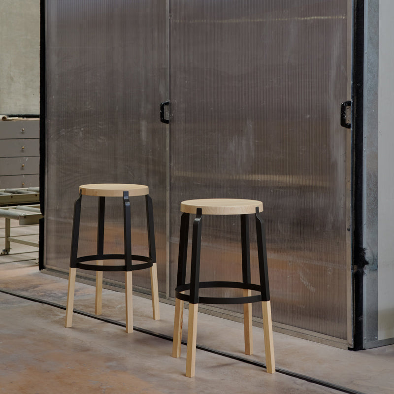Two modern bar stools featuring a natural wood seat and black metal frame, set against a sleek metallic backdrop.