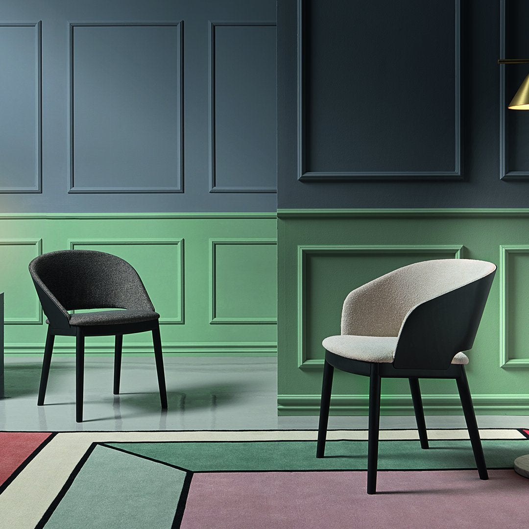Modern chairs featuring a mix of black and cream upholstery against green and blue wall accents, with geometric rug patterns.