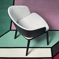 Cozy gray upholstered chair on a colorful geometric-patterned rug in pastel shades of pink, green, and cream.