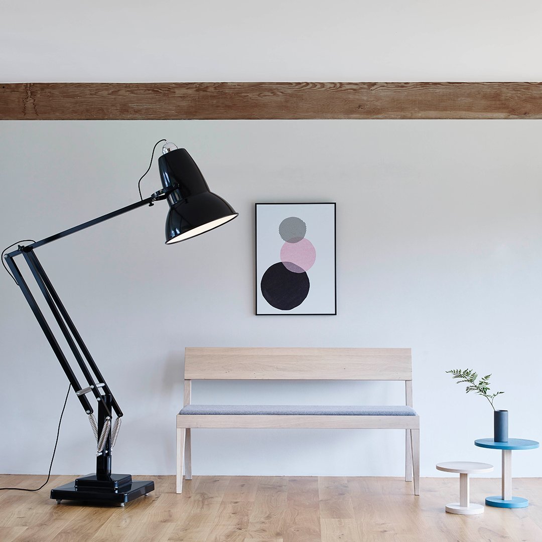 Black lamp, light wood bench with grey cushion, abstract wall art in pink and black circles, blue side table.