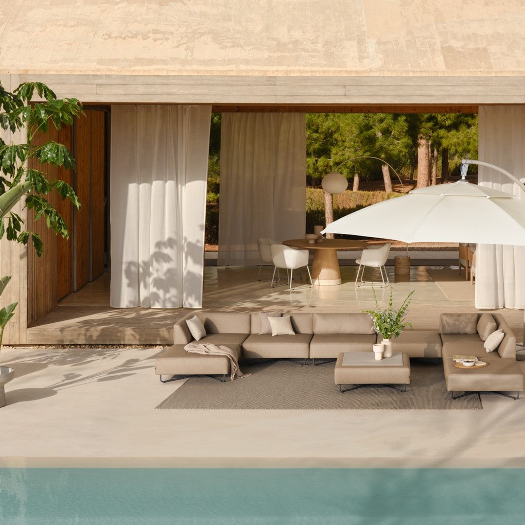 "Neutral-toned outdoor lounge with beige cushions and a white umbrella over a serene, turquoise poolside setting."