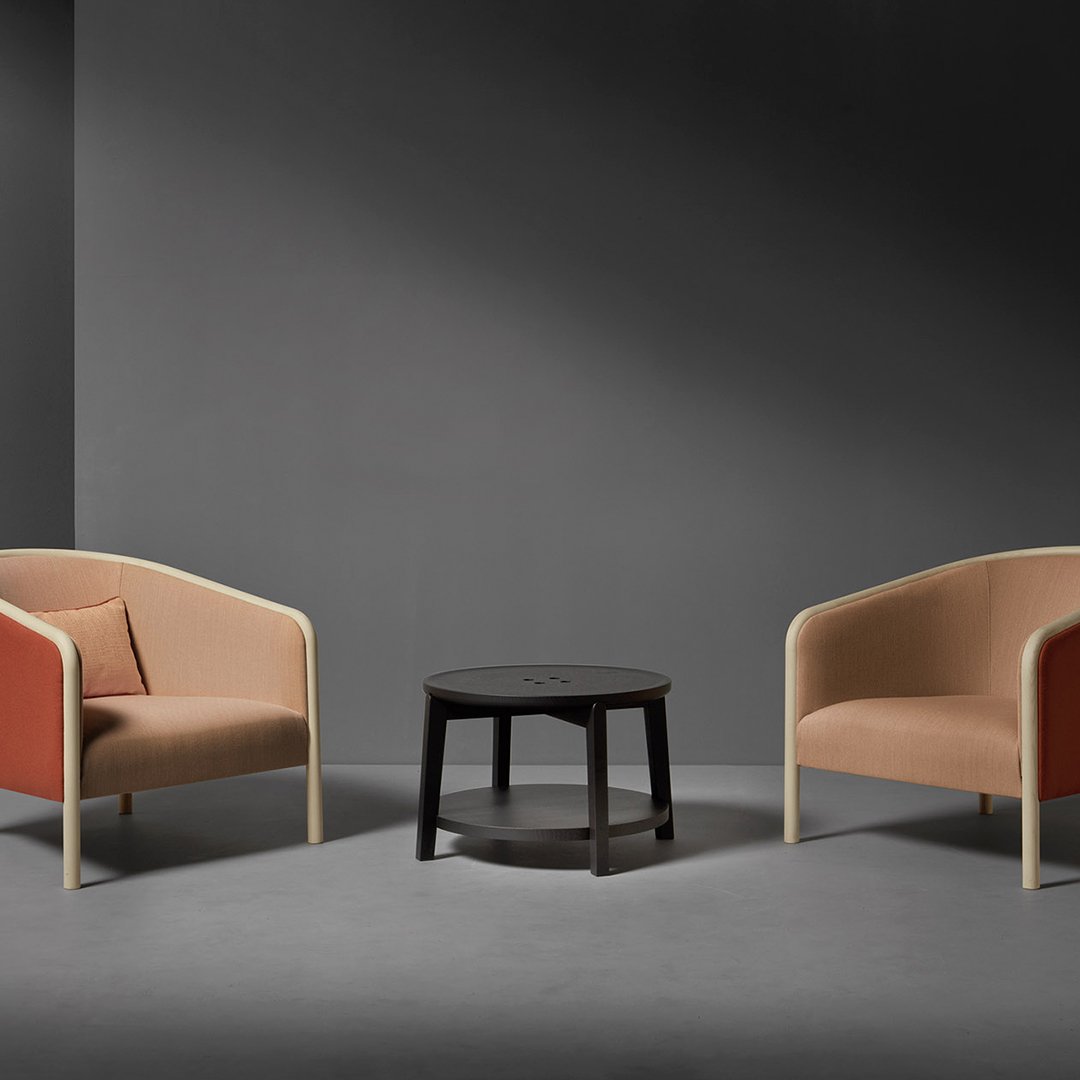 "Two-toned beige and rust armchairs with natural wood legs, paired with a sleek black side table in a minimalist setting."