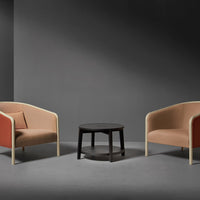 "Two-toned beige and rust armchairs with natural wood legs, paired with a sleek black side table in a minimalist setting."