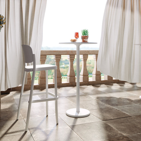 White bistro table and stool set on a stone patio, surrounded by soft white curtains and natural light.