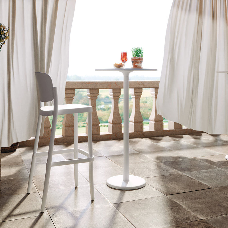 White bistro table and stool set on a stone patio, surrounded by soft white curtains and natural light.