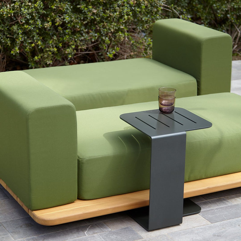 Green cushion sofa with a sleek black side table, featuring a minimalist design against a natural outdoor backdrop.