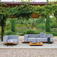 Gray outdoor sofa set with sleek lines and natural wood accents, surrounded by greenery and stone pathways.