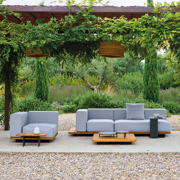 Gray outdoor sofa set with sleek lines and natural wood accents, surrounded by greenery and stone pathways.