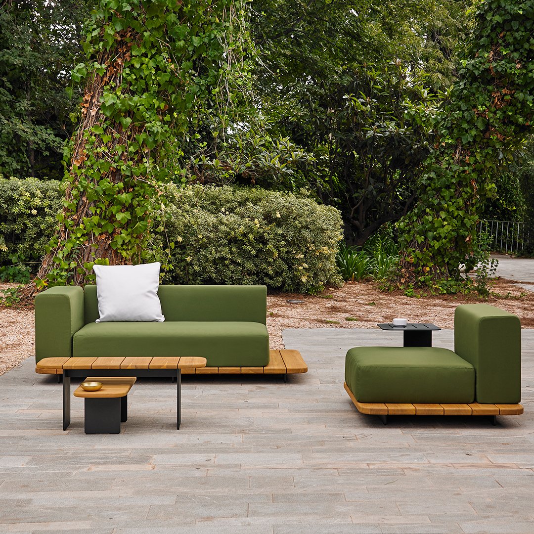 Modern outdoor sofa set featuring deep green cushions and natural wooden accents, set against lush greenery.