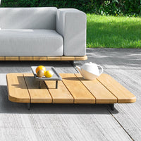 Light natural wood coffee table with horizontal slats, set on a gray stone patio, surrounded by green grass.