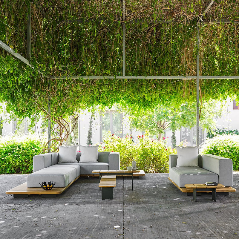 Modern gray outdoor sofa set with wooden accents, surrounded by lush green foliage.