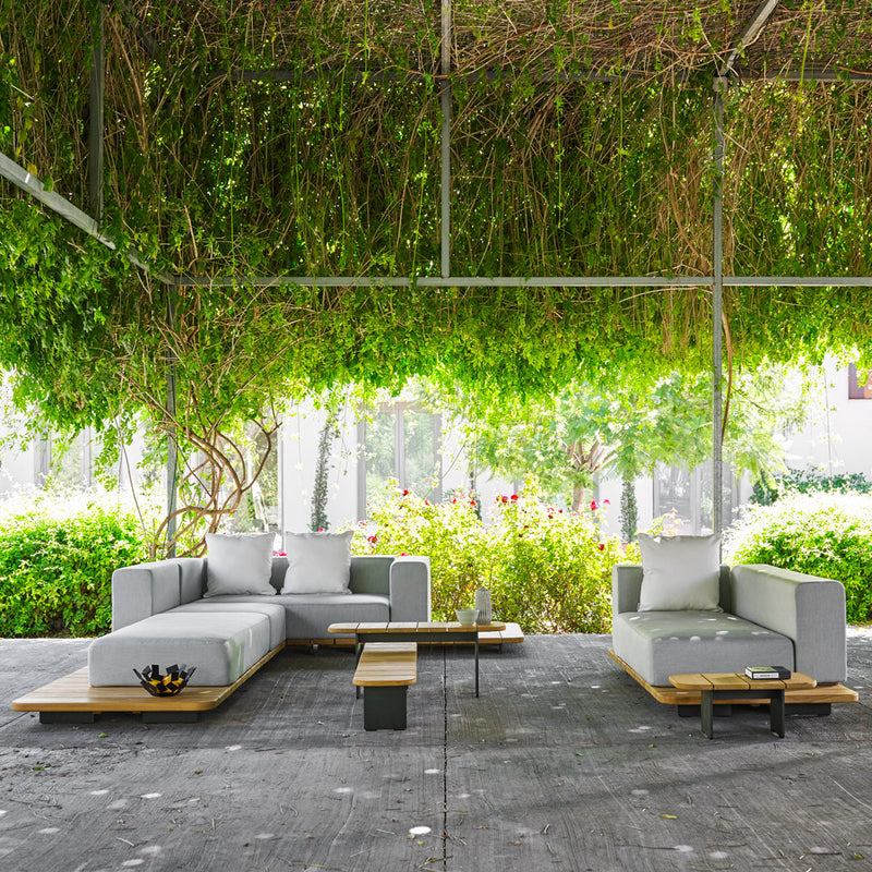 Modern outdoor sofa set in grey with wooden accents, surrounded by lush greenery and vibrant plants.