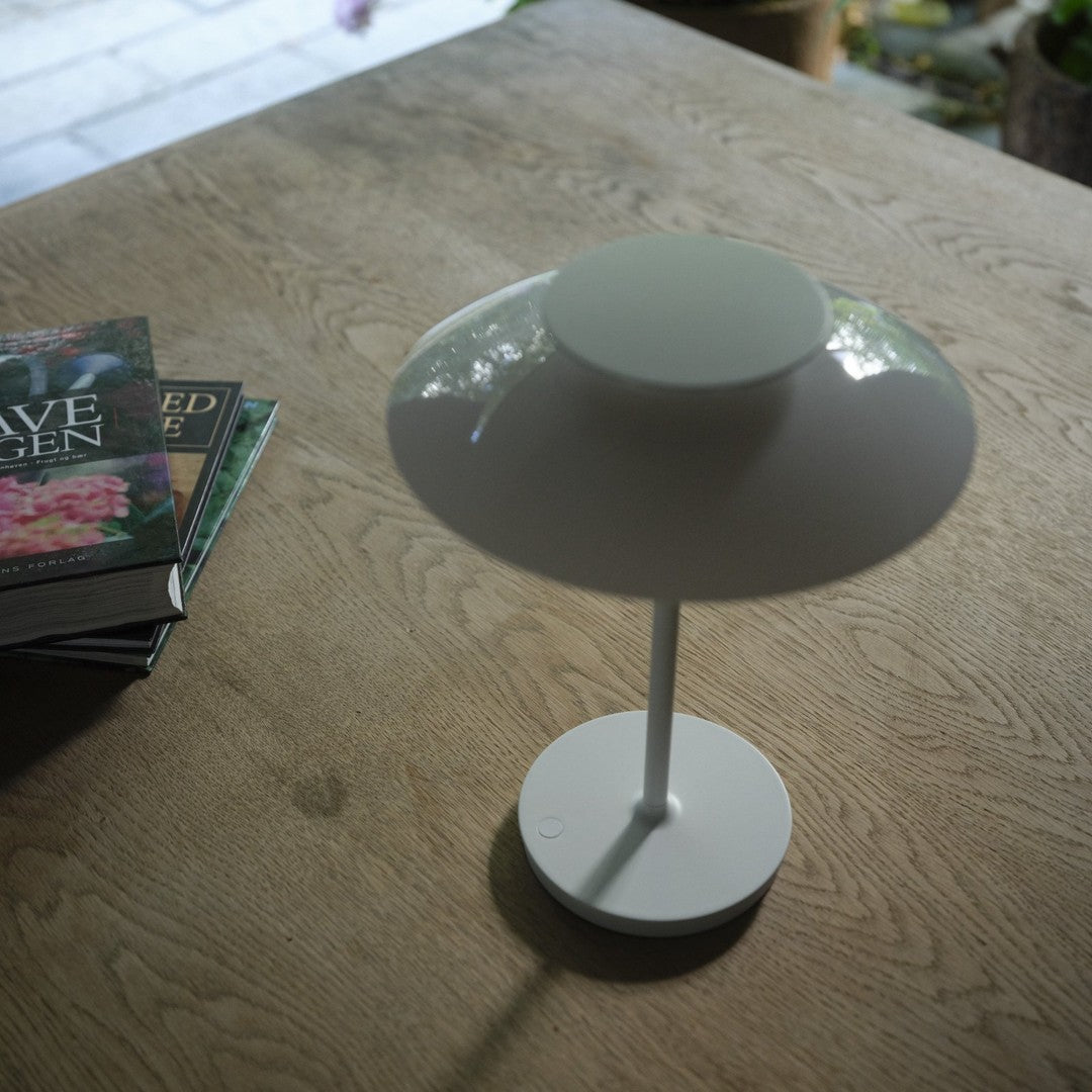 Minimalist white lamp on a wooden table, paired with green and floral-patterned book covers.