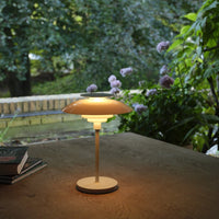 Cream and soft beige lamp with a glossy finish, featuring layered shades for a warm glow against a natural backdrop.