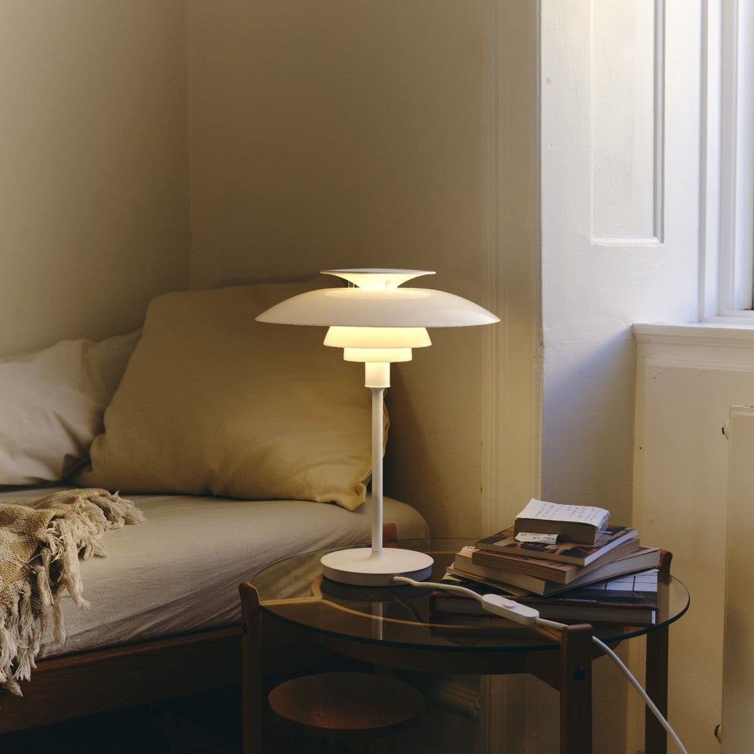 Modern white table lamp with layered shades, soft warm glow, and sleek design against a neutral interior backdrop.